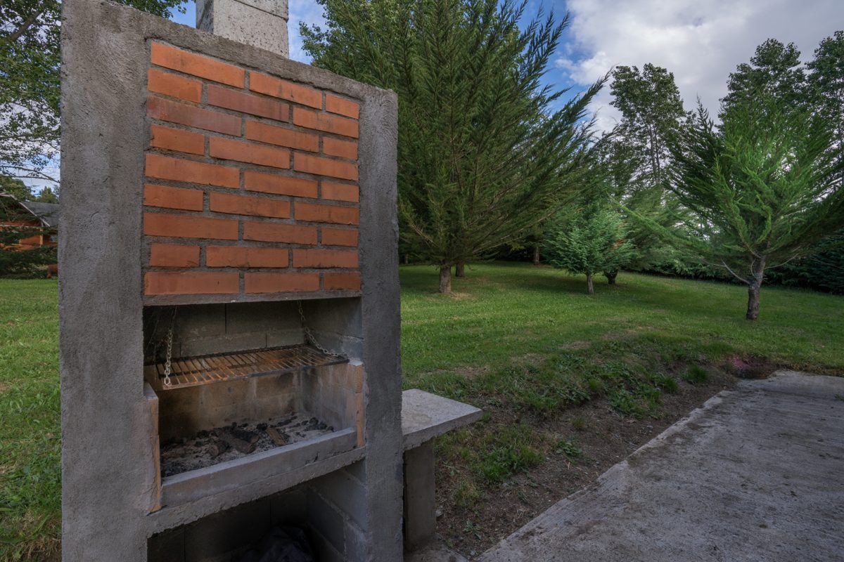 Churrasqueira de tijolos no jardim das cabanas, cercada de árvores