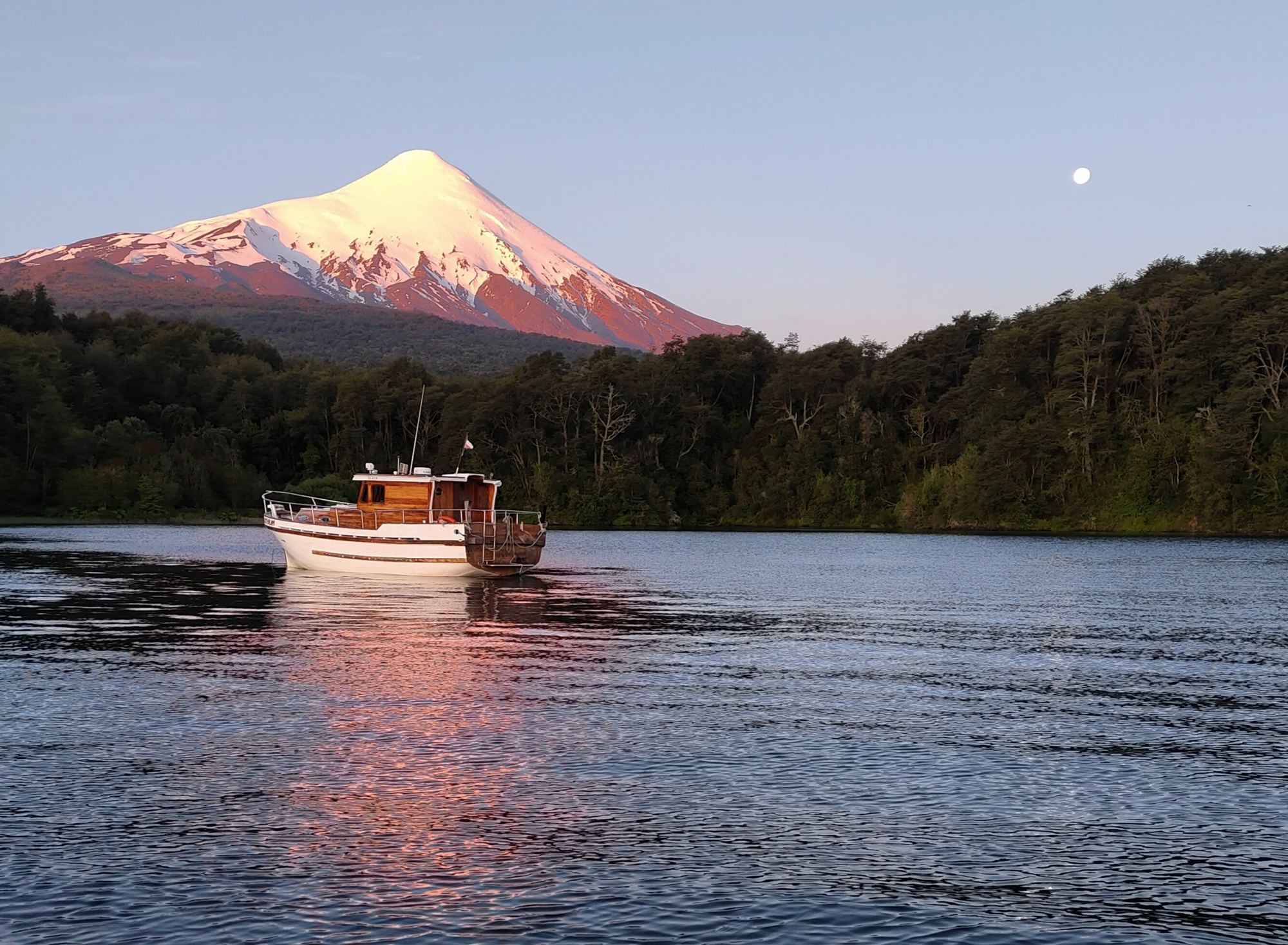 Iate Lithium no setor Ensenada do Lago Llanquihue ao entardecer, com o vulcão Osorno iluminado e a lua cheia