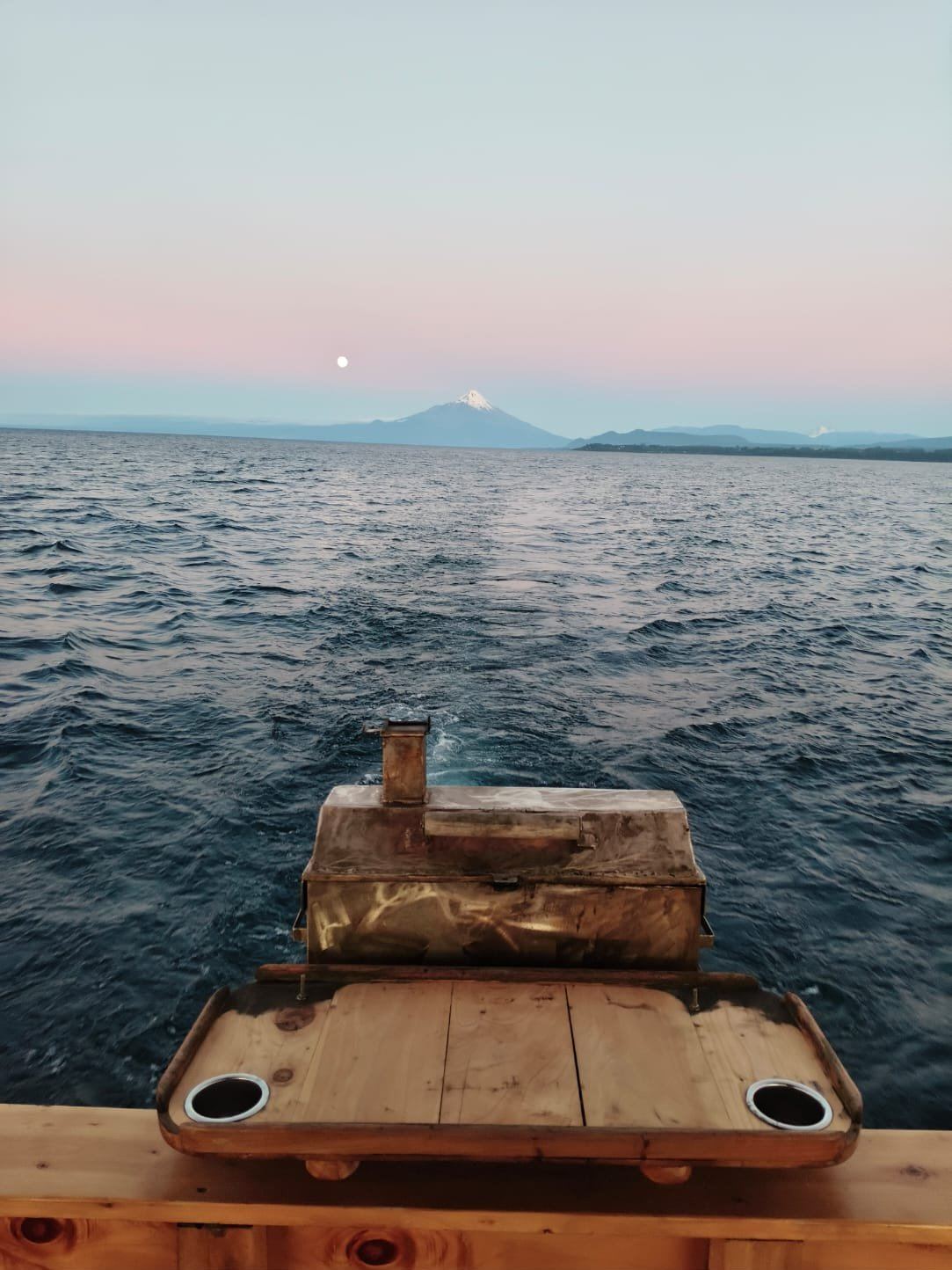 Churrasqueira na popa do Lithium navegando ao entardecer, com o vulcão Osorno e a lua ao fundo
