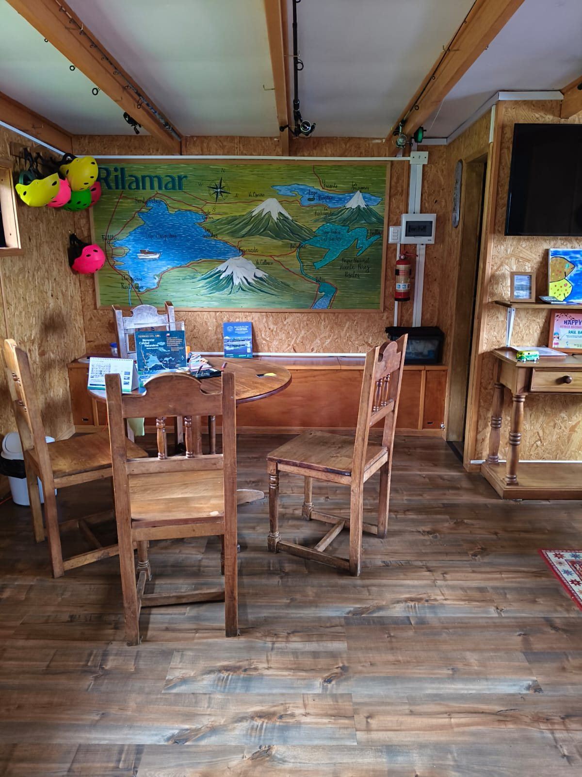 Interior do escritório com um grande mapa pintado do Lago Llanquihue e seus vulcões, mesa e cadeiras de madeira