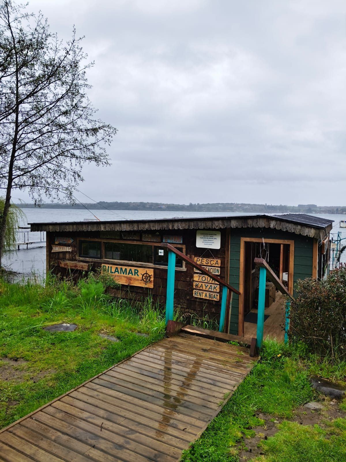 Passarela de madeira até o escritório da Rilamar, com placas de pesca, navegação, tour, caiaque e aluguel de barcos, junto ao lago
